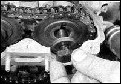 7. Удерживая распредвал ключом за лыски в передней части, отверните болты крепления звездочек…